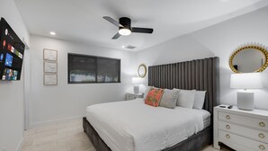 Quarto moderno com cama, mesas de cabeceira, ventoinha no teto, janela com persianas e espelho fixado na parede.