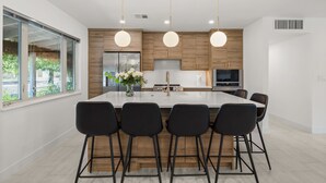 Uma cozinha moderna com ilha central, banquetas pretas, armários de madeira e eletrodomésticos de aço inoxidável.