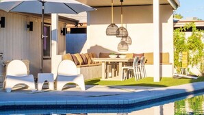 Uma área moderna de piscina ao ar livre com um espaço de estar coberto, uma mesa e cadeiras.