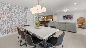 Uma sala de jantar moderna com uma mesa branca, cadeiras pretas e uma planta central.