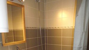 Een badkamer met een wit wastafel, een houten opbergmeubel, een spiegel, een douche en een bad.