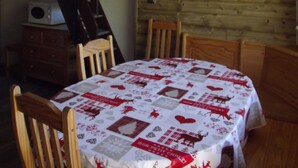Een eethoek met een tafel, gedekt met een tafelkleed met dessin, houten stoelen, een houten wand met een decoratie in de vorm van een hart, en een trap met een houten leuning.