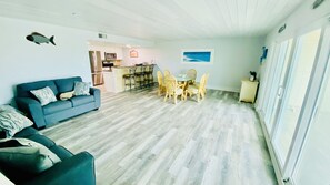 Una sala de estar con un sofá azul, una mesa de comedor con sillas y una cocina al fondo.