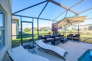 A covered outdoor patio with lounge chairs, a pool, and a view of a residential area.