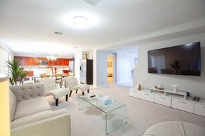 A modern living room with a glass coffee table, a large flat-screen TV, and a sofa.