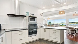 Een moderne keuken met witte kasten, roestvrijstalen apparatuur en uitzicht op de natuur.