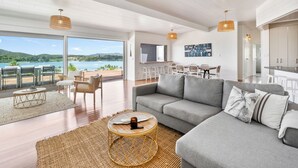 Een ruime woonkamer met een grijze bank, een rieten salontafel en grote ramen met uitzicht op zee.