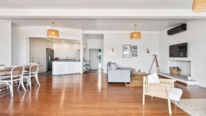 Een ruime woonkamer met een houten vloer, witte meubels en hanglampen.