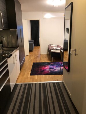 Quarto compacto com cozinha compacta, cama e tapete com tema espacial, e porta que dá para outro cômodo.