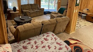 Una sala de estar acogedora con un sofá, un sillón reclinable y una mesa de centro. Hay un televisor y una lámpara sobre una mesita auxiliar.