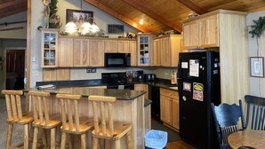 Una cocina con armarios de madera, un refrigerador negro, un microondas y una barra con taburetes de madera.