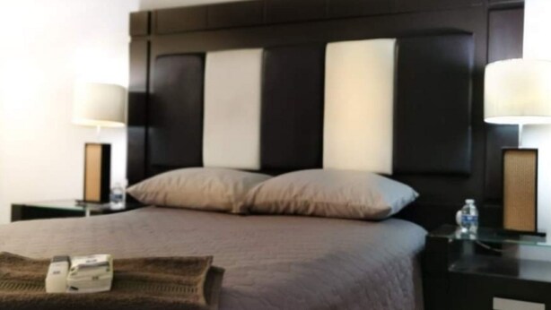 A hotel room with a large bed, two bedside tables, and a headboard with vertical panels. - Casa Dahlia Queretaro (Querétaro)