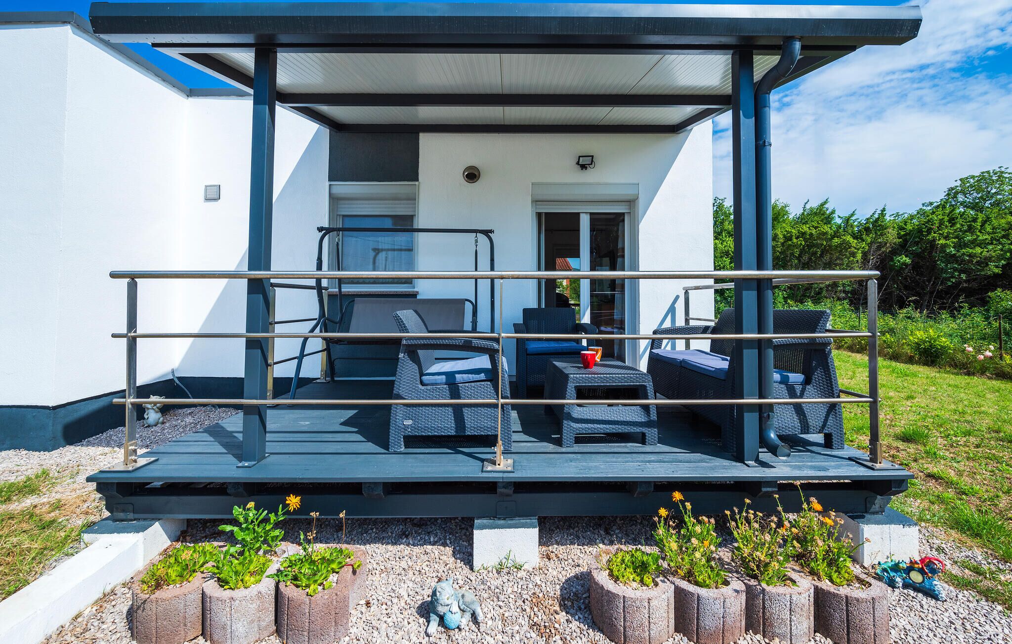 A covered outdoor seating area with chairs and tables, a metal railing, and planters with flowers.