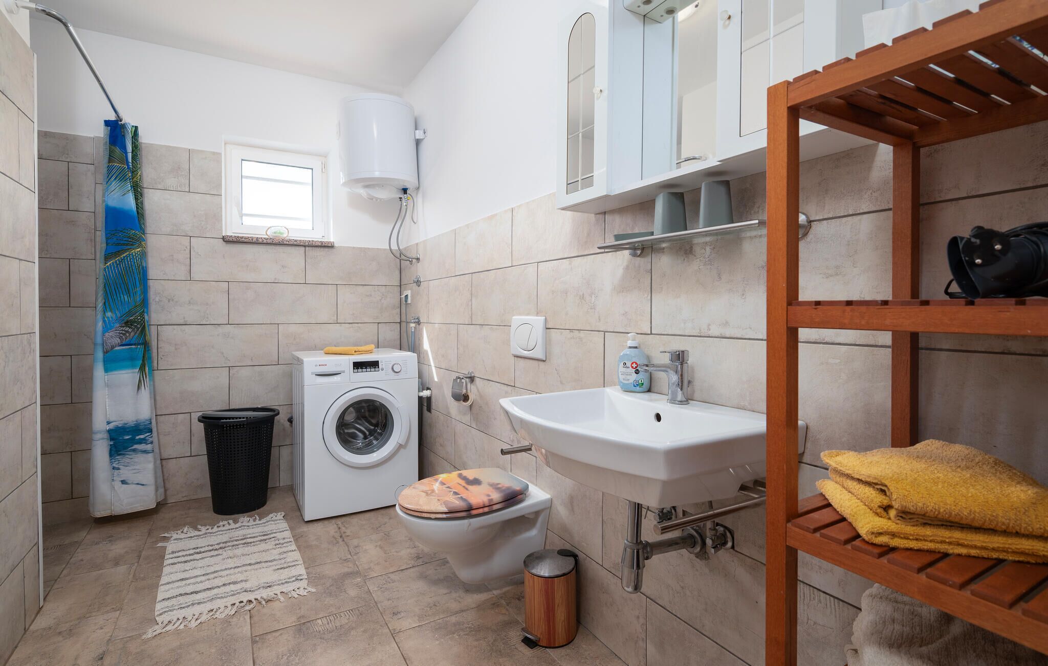 A compact bathroom with a washing machine, toilet, sink, and a wooden shelf with towels.