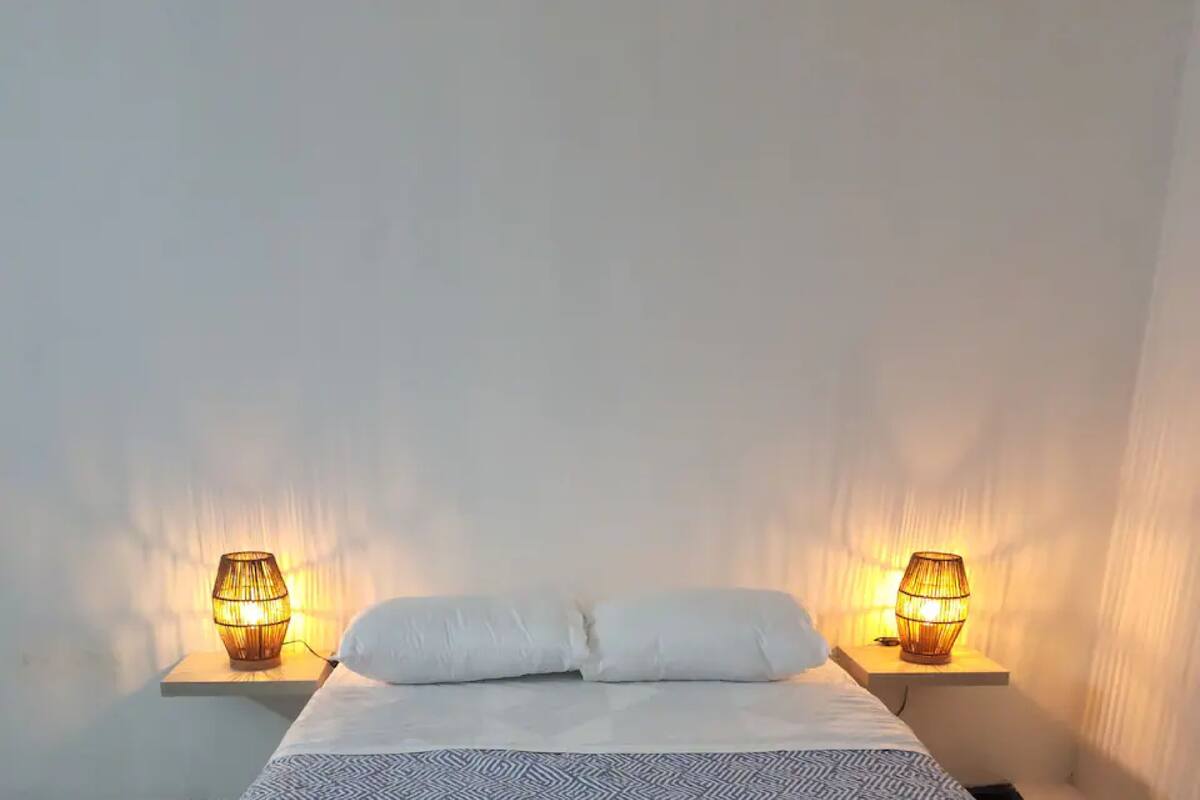 A bed with white bedding, flanked by two bedside tables with lamps.
