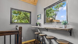 Una cocina moderna con taburetes de bar, encimera de madera y grandes ventanales con vistas a un jardín.