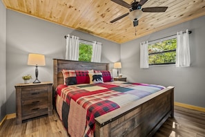 A bedroom with a wooden bed, two nightstands, a ceiling fan, and windows with curtains.