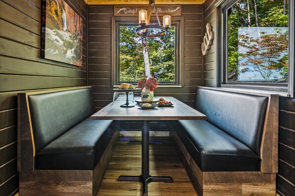 A cozy restaurant interior with wooden walls, a large window with a view of trees, and a table set with food and drinks.