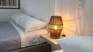 Une chambre avec deux lits, une table de chevet avec une lampe et une fenêtre avec des barreaux.
