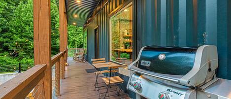 Une terrasse extérieure équipée d’un barbecue Weber Spirit, de chaises en bois et offrant une vue sur la verdure environnante.