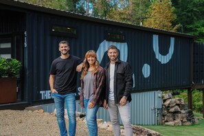 Three people standing in front of a building with a large 'U' painted on it. - Shipyard 2.0 | Hot Tub, Waterfall with Daybed, Fire Pit + Hammock! (Columbus)