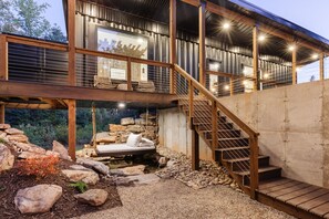 A modern two-story building with a wooden staircase and outdoor seating area. - Shipyard 2.0 | Hot Tub, Waterfall with Daybed, Fire Pit + Hammock! (Columbus)