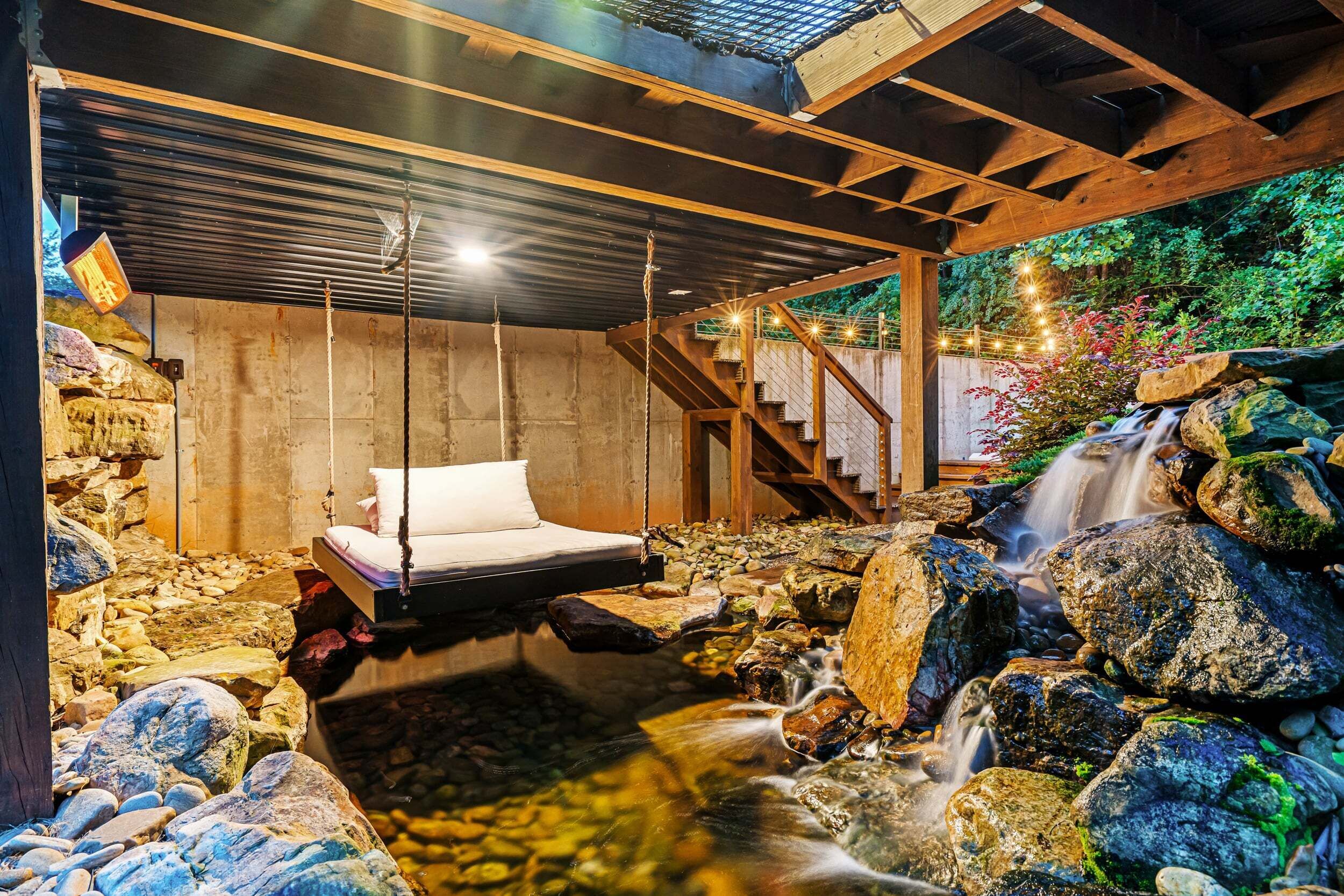 Una cabana de fusta rústica amb un llit hamaca, una paret de pedra i una cascada.