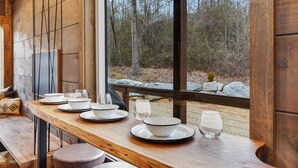 Ett matbord i trä med vita tallrikar och skålar, placerat framför ett fönster med utsikt över träd och klippor.