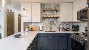 Una cucina moderna con mobili blu scuro, piani di lavoro bianchi e una parete di fondo in marmo.