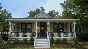 Una casa a due piani con un portico, un vialetto in mattoni che conduce all'ingresso e un piccolo giardino antistante con siepi e prato.