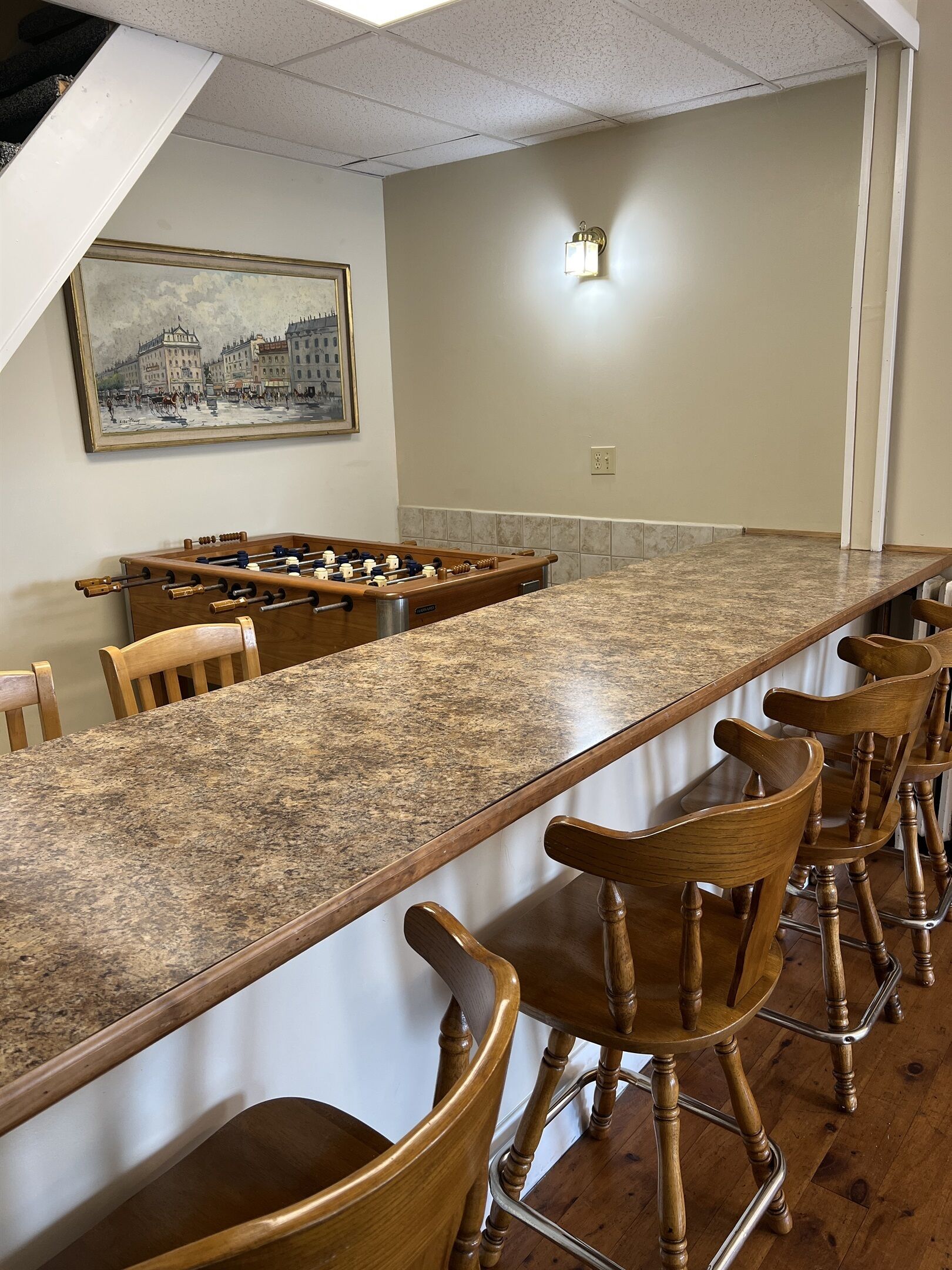A bar area with a long granite countertop, wooden chairs, and a foosball table.
