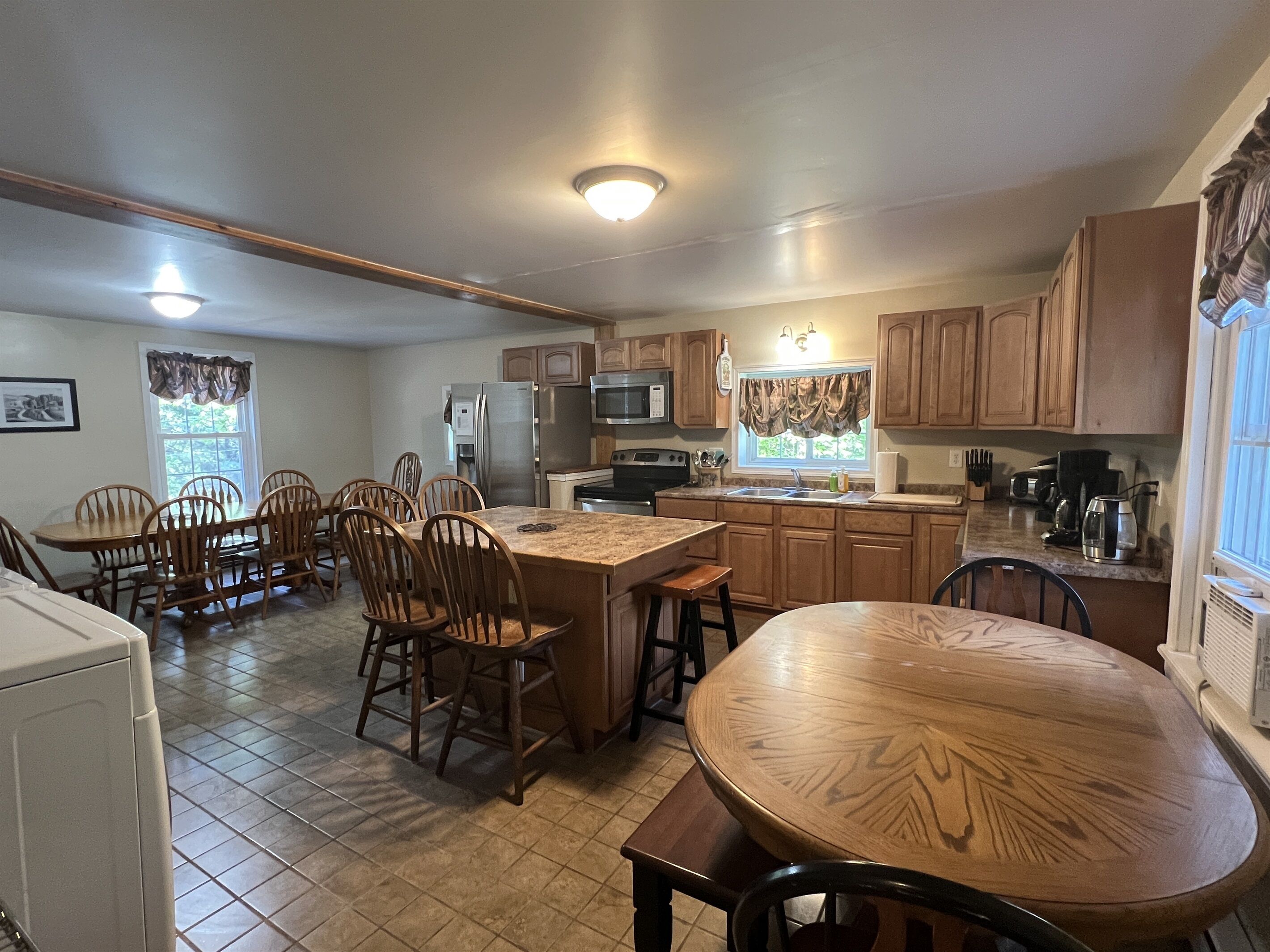 A kitchen with wooden cabinets, a central island, and a dining area with chairs.