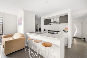 Una cocina moderna con armarios blancos, una isla central con taburetes y un horno empotrado.
