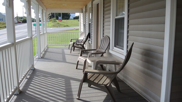 A covered porch with two Adirondack chairs, a wooden ceiling, and a view of a road and greenery. - Alan's Corner - 4 bedroom / 4 bath, pool, less than 5 minutes to Dreams Park (Cooperstown)
