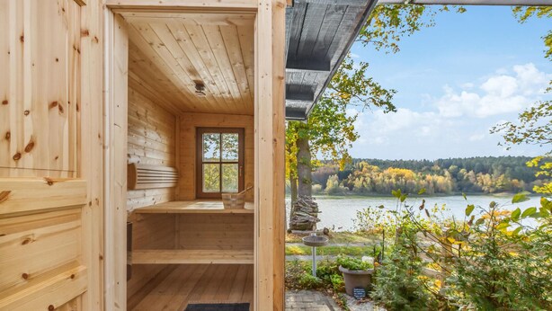 A wooden cabin with a bench and a window overlooking a lake and forest.