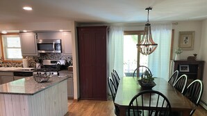 A modern kitchen with a central island, a dining area with a wooden table and chairs, and a chandelier.