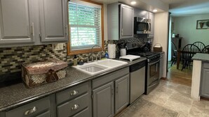 A kitchen with grey cabinets, a sink, a stove, and a window with blinds.