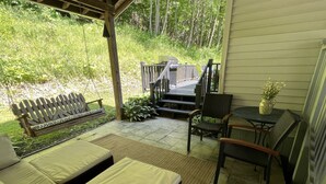 A covered patio with a sofa, chairs, a small table, and a grill.