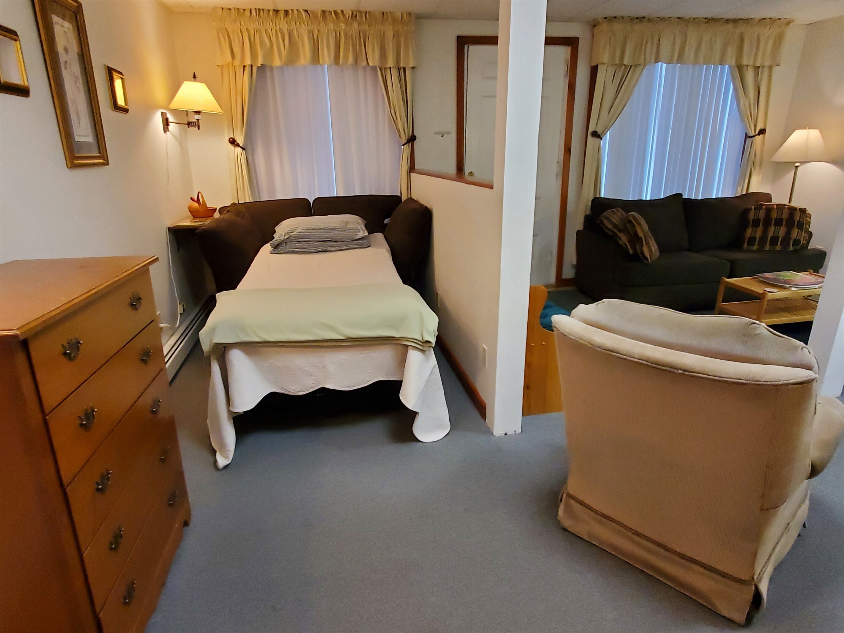 A hotel room with a bed, a chair, a dresser, and a sofa.