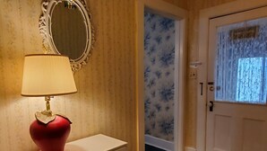 A hallway with a white cabinet, a red lamp, a mirror, and a door with a floral curtain. - Apple Tree Apt 2, Charming 2nd fl apt, under 5 minutes to Dreams Park (Milford)