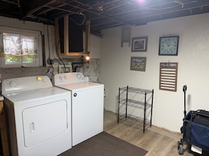 A laundry room with a washing machine, a dryer, a metal shelf unit, and a wall-mounted clock.