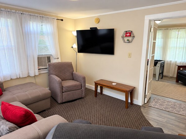 A living room with a sofa, armchair, and a flat-screen TV mounted on the wall. - Apple Tree Oneonta NEW Renovation, Under 1 mile to All Star Village, 2 bdrm home (Oneonta)