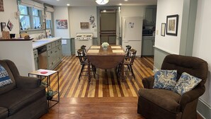 Un coin repas avec une table et des chaises en bois, une cuisine équipée d’une cuisinière et d’un réfrigérateur, et un salon avec un canapé et un fauteuil.