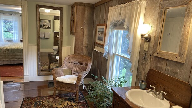 Une salle de bain rustique avec un meuble-lavabo en bois, une chaise en osier, un tapis à motifs et une plante en pot.