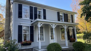 Une maison à deux étages avec un porche, un revêtement extérieur blanc et des volets noirs.