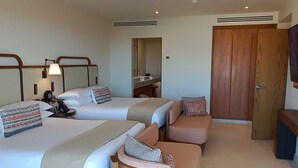 A spacious hotel room with two large beds, a wooden bench, a sofa, and a wardrobe.