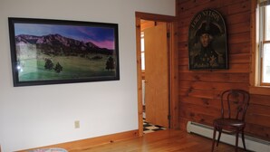 Une pièce comprenant un lit, une chaise en bois, un tableau représentant un paysage encadré et un portrait accroché au mur.