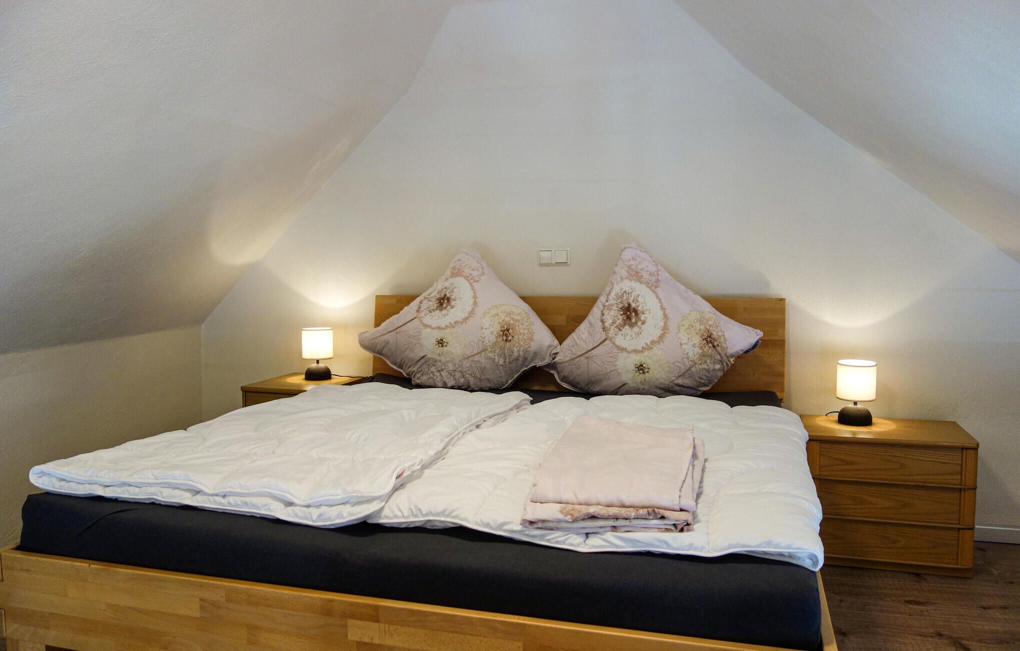 A neatly made bed with two pillows and two bedside tables with lamps, in a room with sloped ceilings.