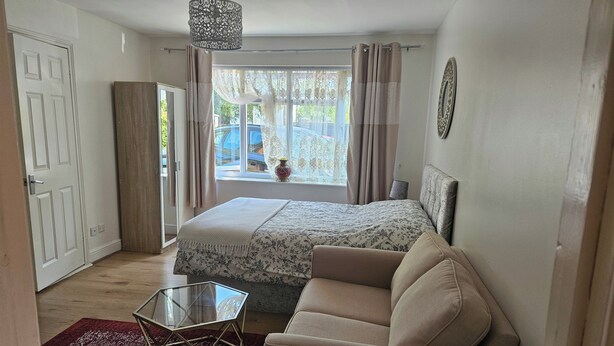 A bedroom with a bed, a sofa, a glass table, a red rug, a window with curtains, and a hanging light fixture. - Lovely Studio in Town Centre (Reading)