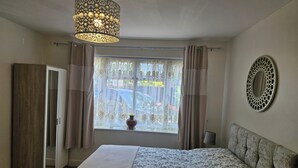 A bedroom with a bed, a wardrobe, a window with curtains, a hanging light fixture, and a wall mirror. - Lovely Studio in Town Centre (Reading)